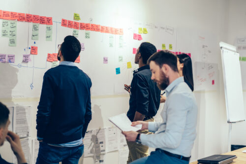 Professional team of young people in formal wear cooperating on creating project using colorful text notes glued on wall in office.Group of students learning foreign words on stickers during lesson