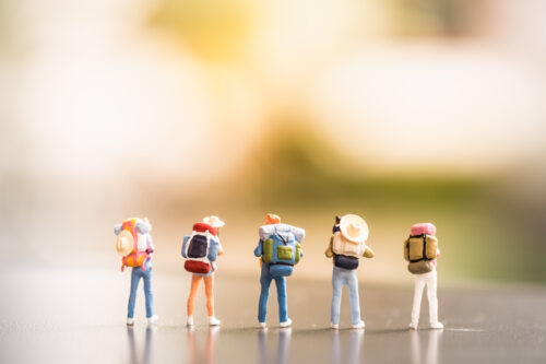 Travelling concepts. Group of traveler miniature mini figures with backpack and hat stand and walking on ground