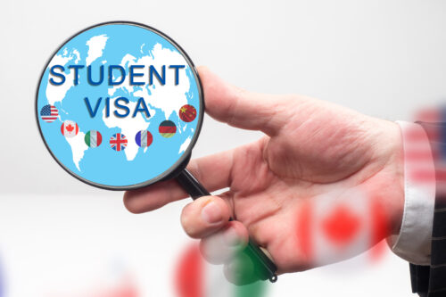Student visa. Search for student visa information. Applying for study at a foreign university. Human hand with magnifying glass. World map and flags as a symbol of study abroad. University abroad