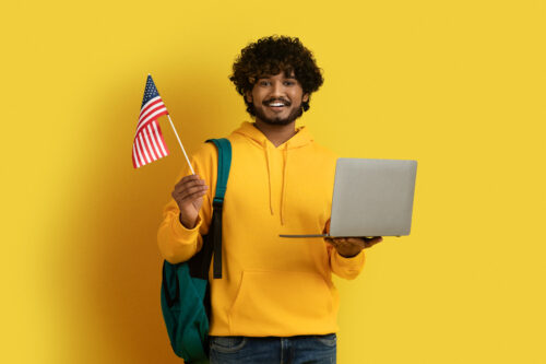 Happy young guy holding laptop and flag of US
